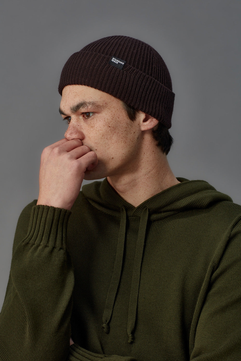 Man wearing a dark beanie and green hoodie against a gray background