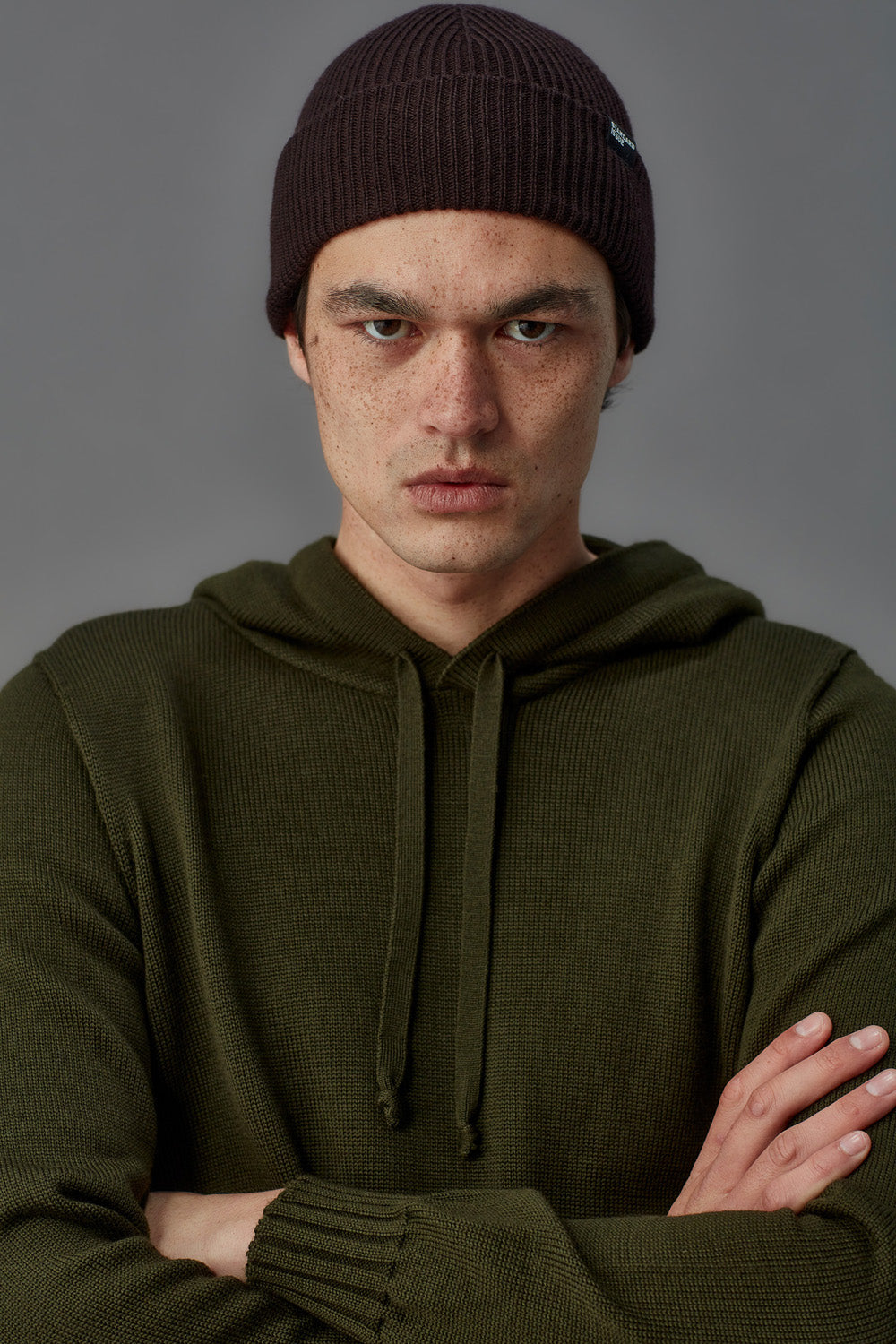 Person wearing a dark beanie and green hoodie against a gray background