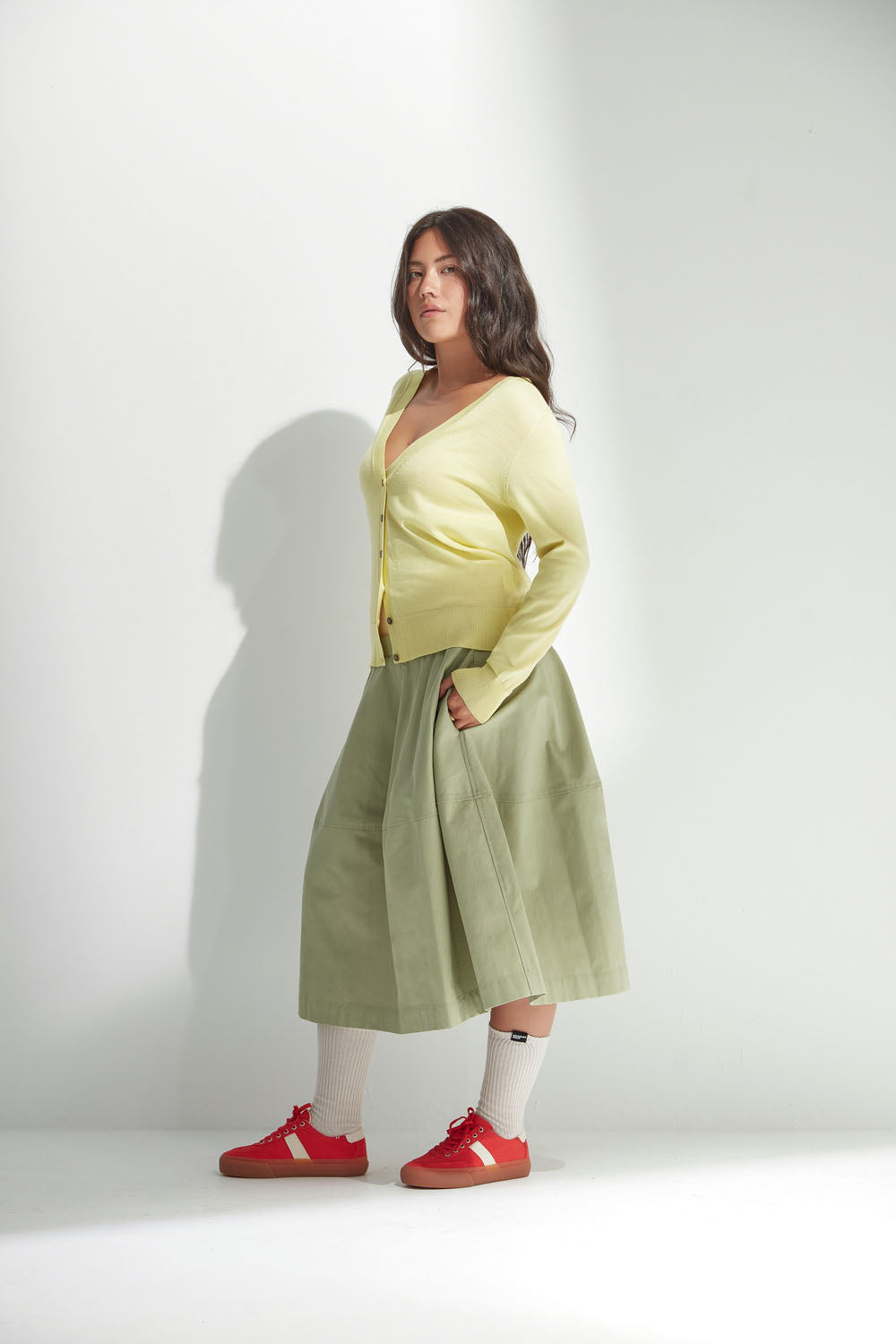 Woman wearing a yellow cardigan, green skirt, and red shoes on a white background