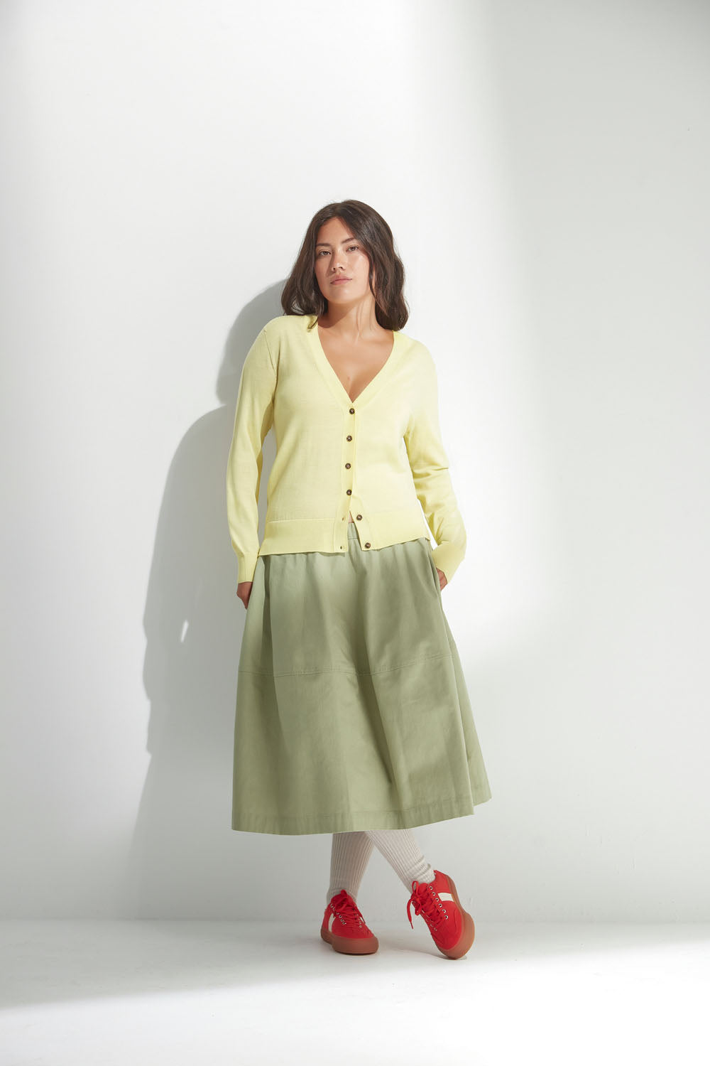 Woman wearing a light yellow cardigan and green skirt on a white background