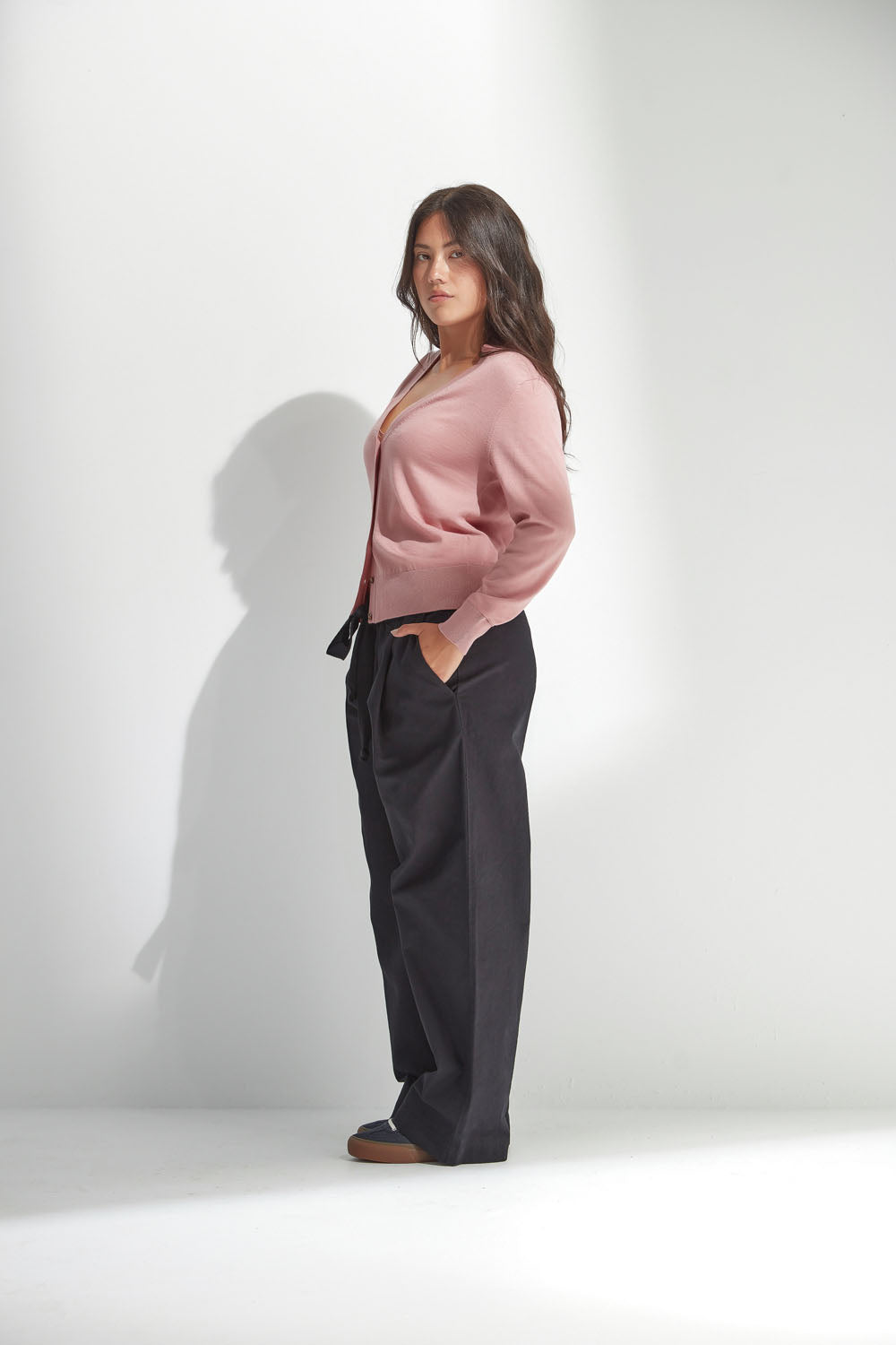 Woman wearing a pink sweater and black pants against a white background