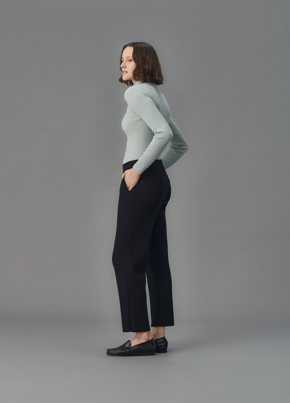 Woman wearing a light blue ribbed top and black pants against a gray background