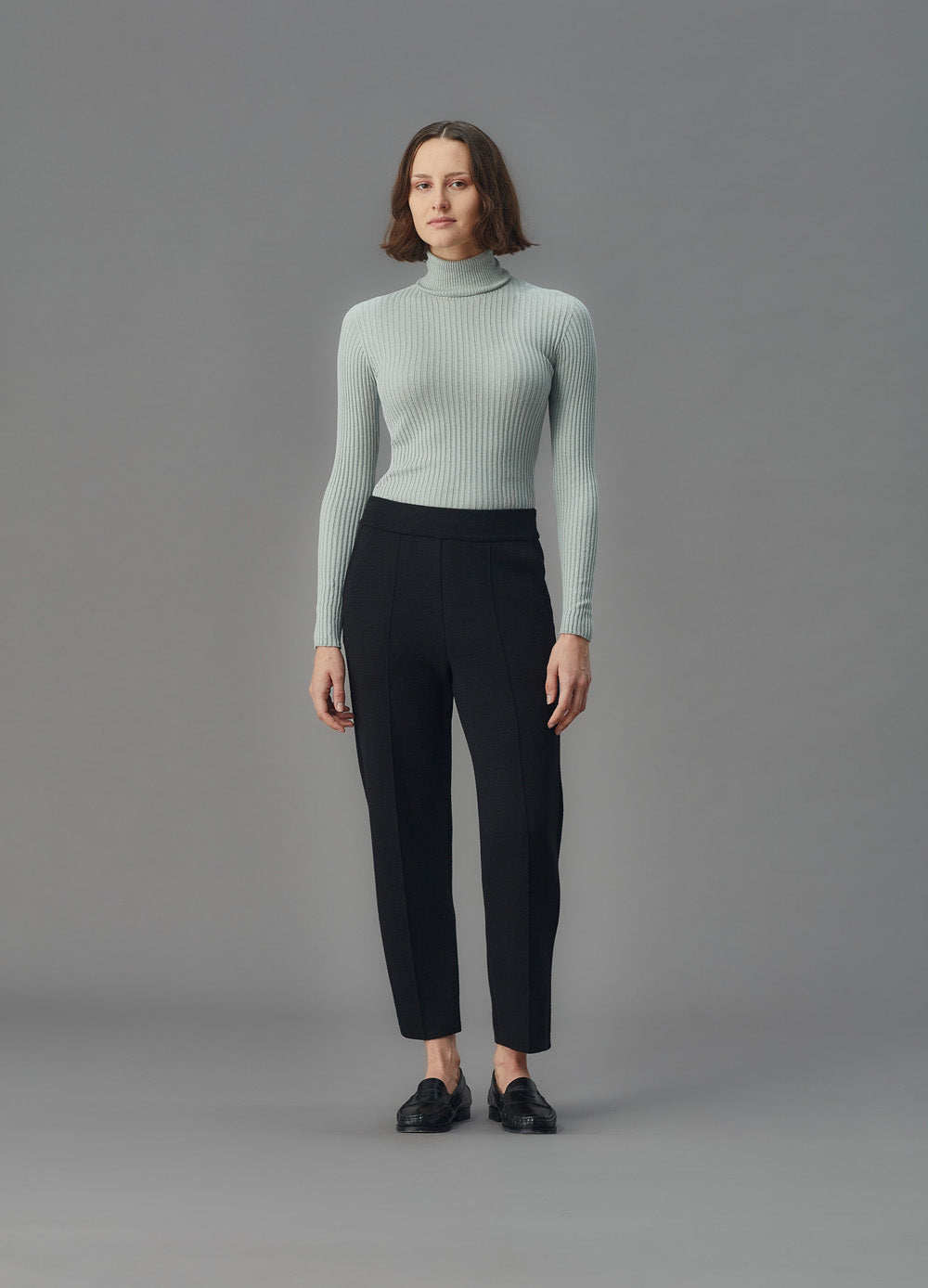 Woman wearing a light blue ribbed top and black pants against a gray background