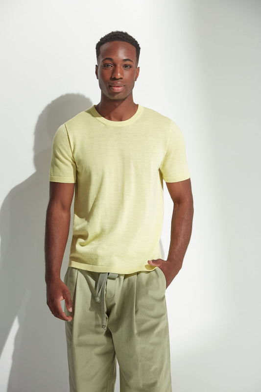 Man wearing a light yellow t-shirt and green pants against a white background