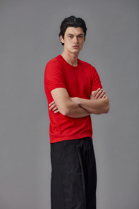 Man wearing a red merino shirt and black pants against a gray background