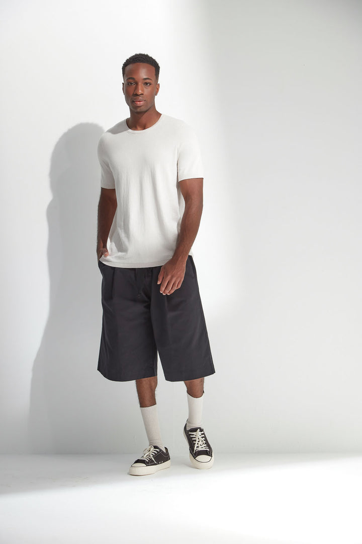Man wearing a white t-shirt, dark shorts, and black sneakers on a white background