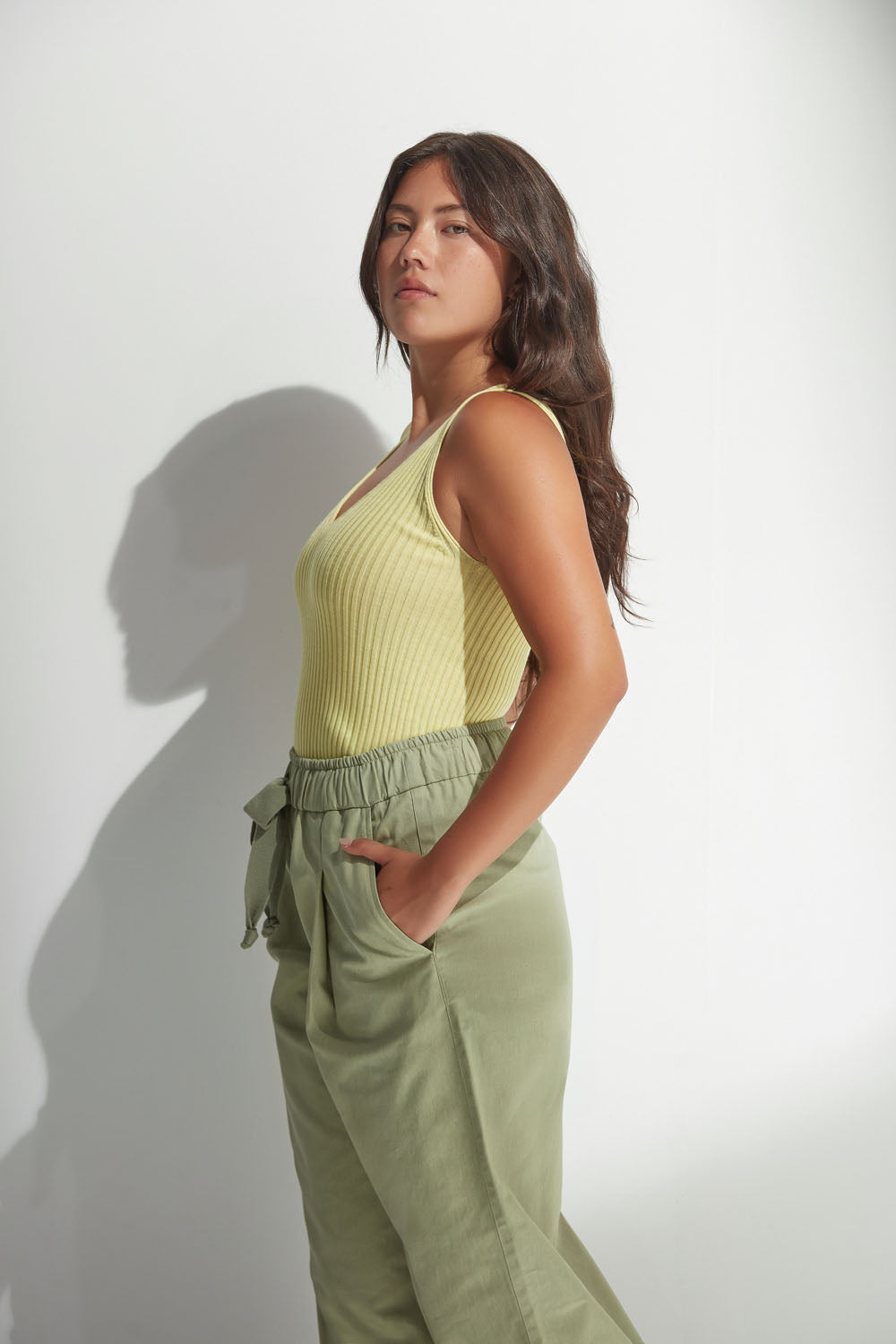 Woman wearing a yellow sleeveless top and green pants against a white background