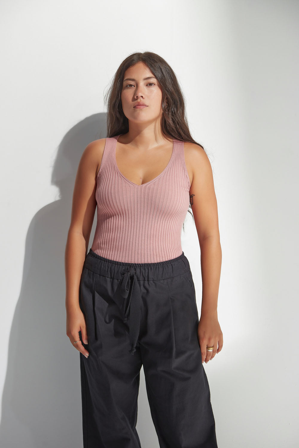 Woman wearing a pink ribbed tank top and black pants against a white background