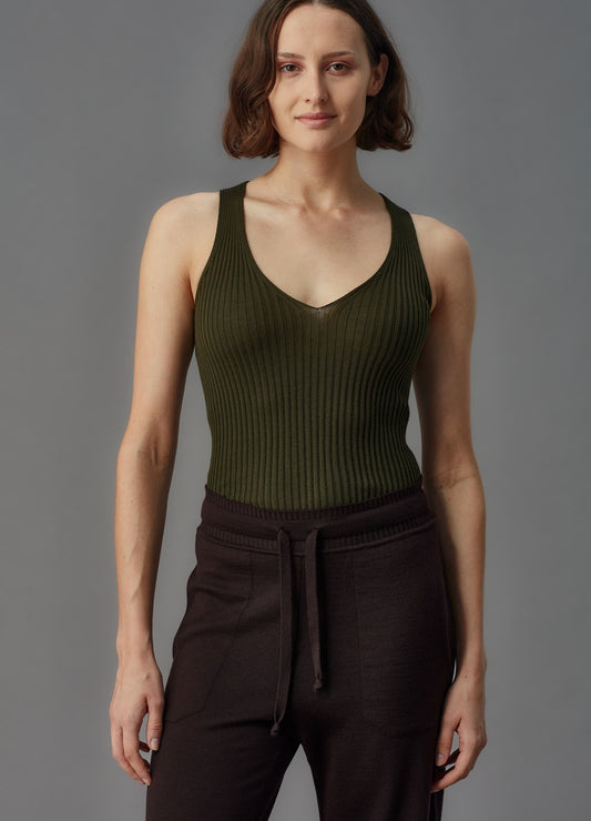 Woman wearing a green ribbed tank top and brown pants against a gray background