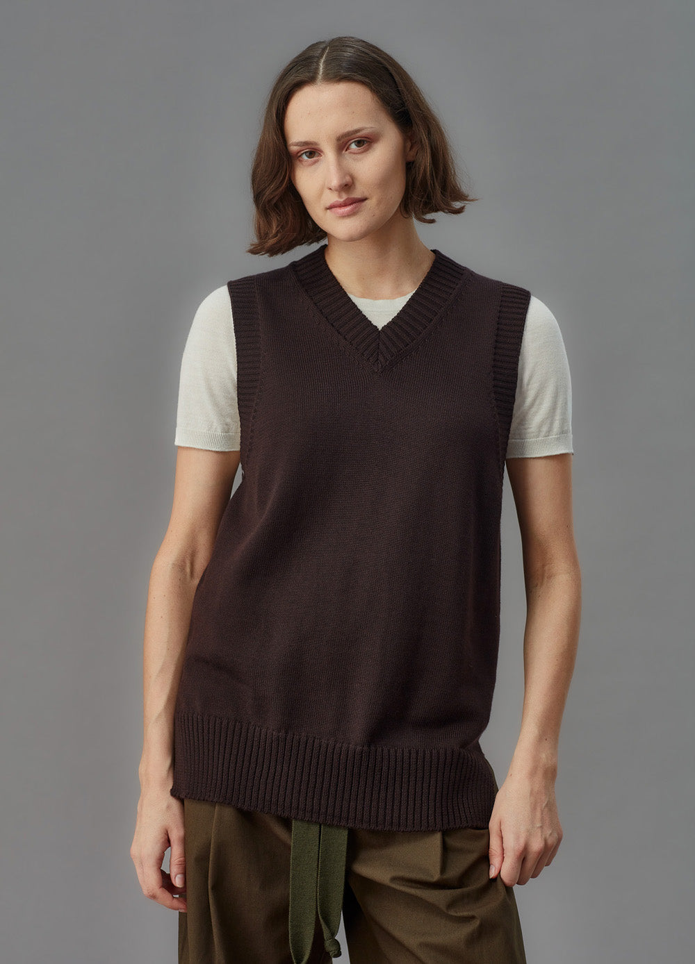 Person wearing a brown knitted sweater vest over a white shirt on a gray background