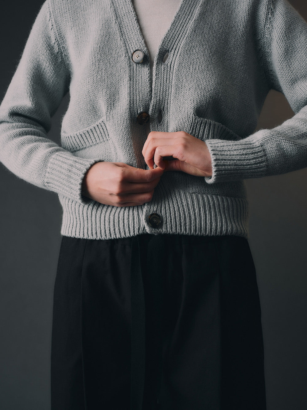 Person wearing a light blue cardigan with black buttons against a dark background