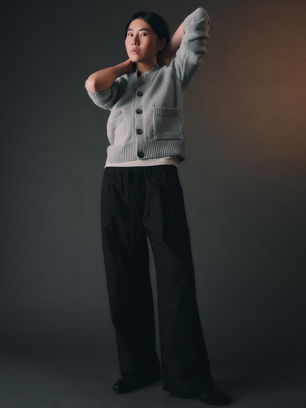 Person wearing a light blue cardigan with black buttons against a dark background