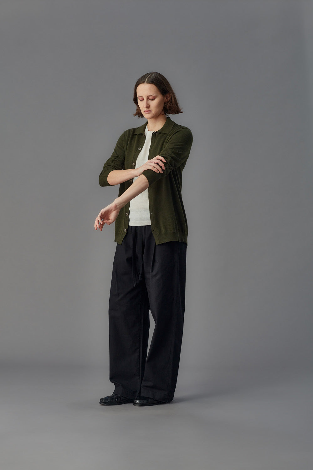 Person wearing a green shirt and black pants on a gray background