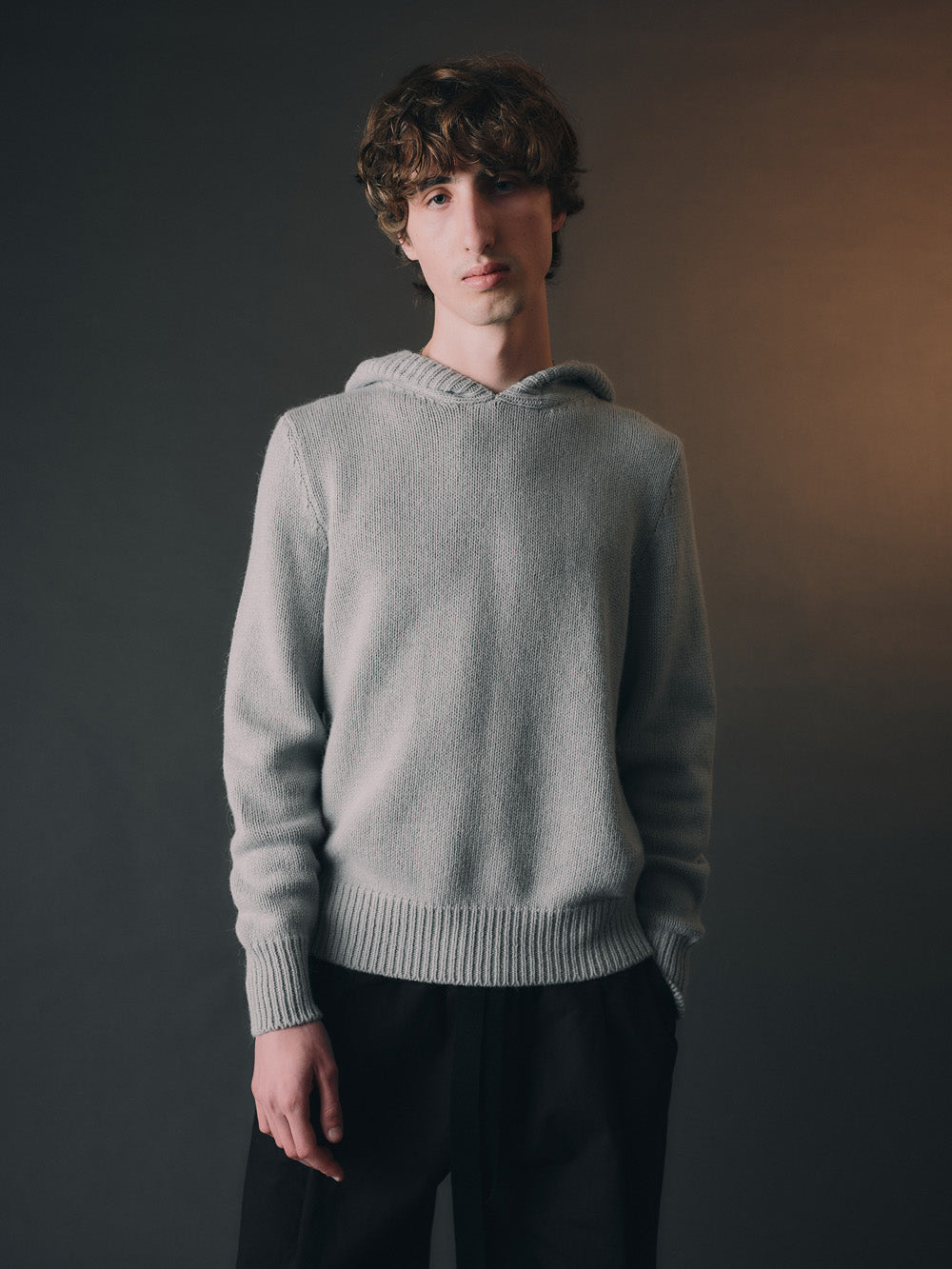 Person wearing a light blue hooded knit sweatshirt against a dark background