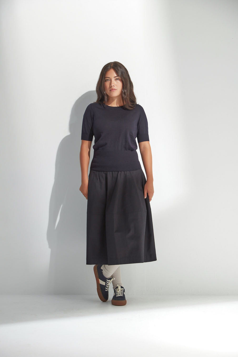 Woman wearing a navy top and skirt against a white background