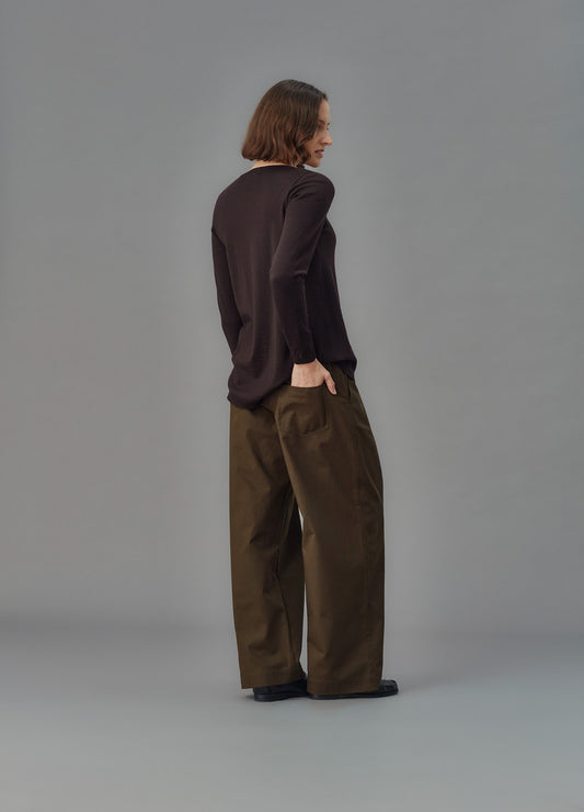 Person wearing a dark sweater and green pants against a gray background