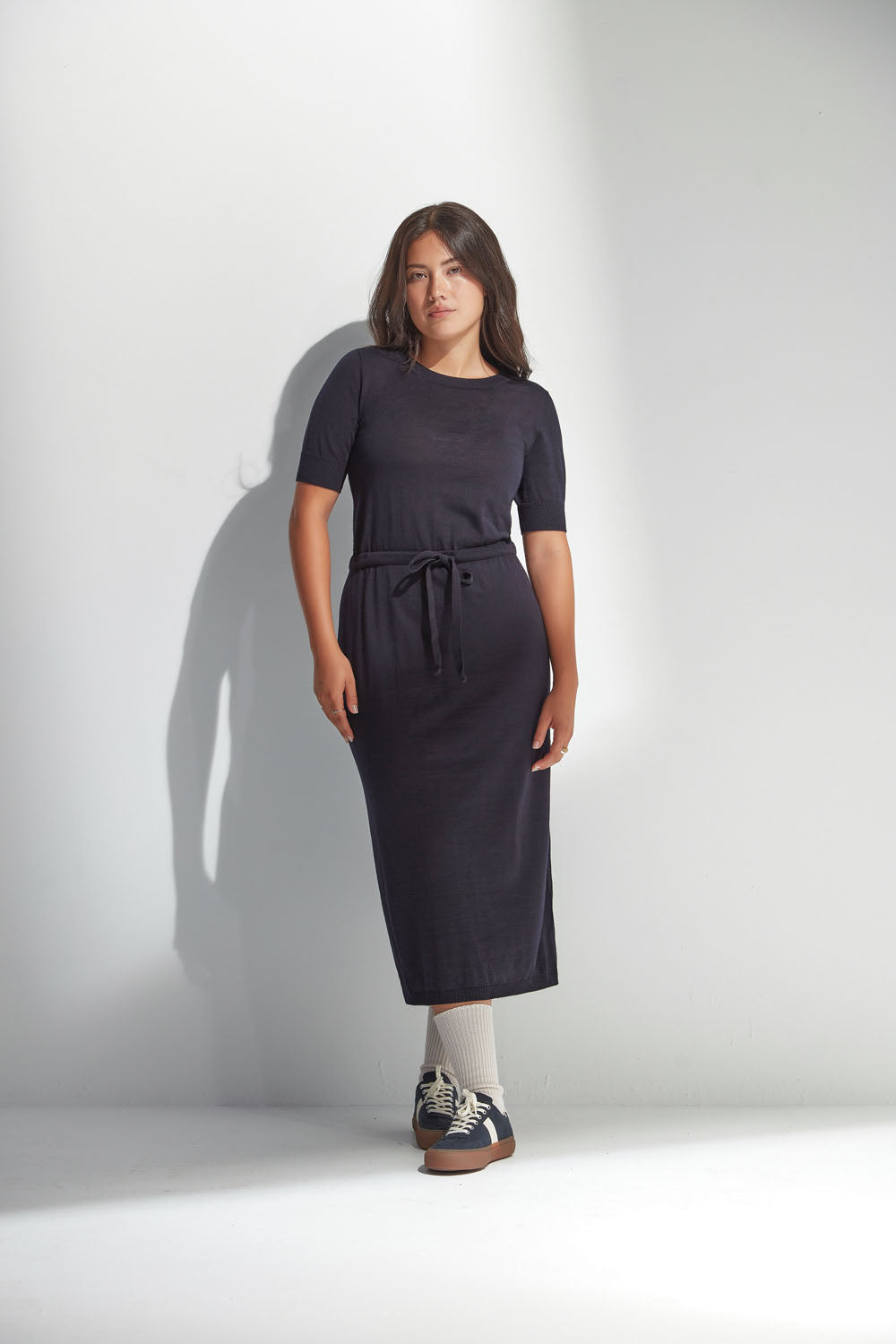 Woman wearing a navy dress standing against a white background