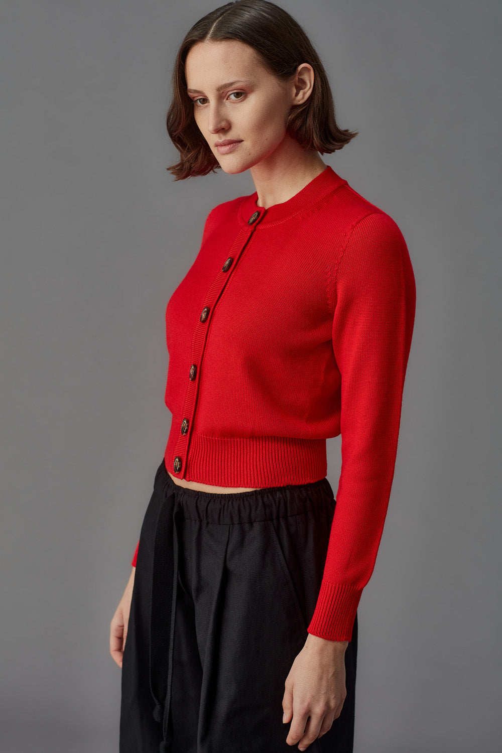 Woman wearing a red cardigan with black buttons against a gray background