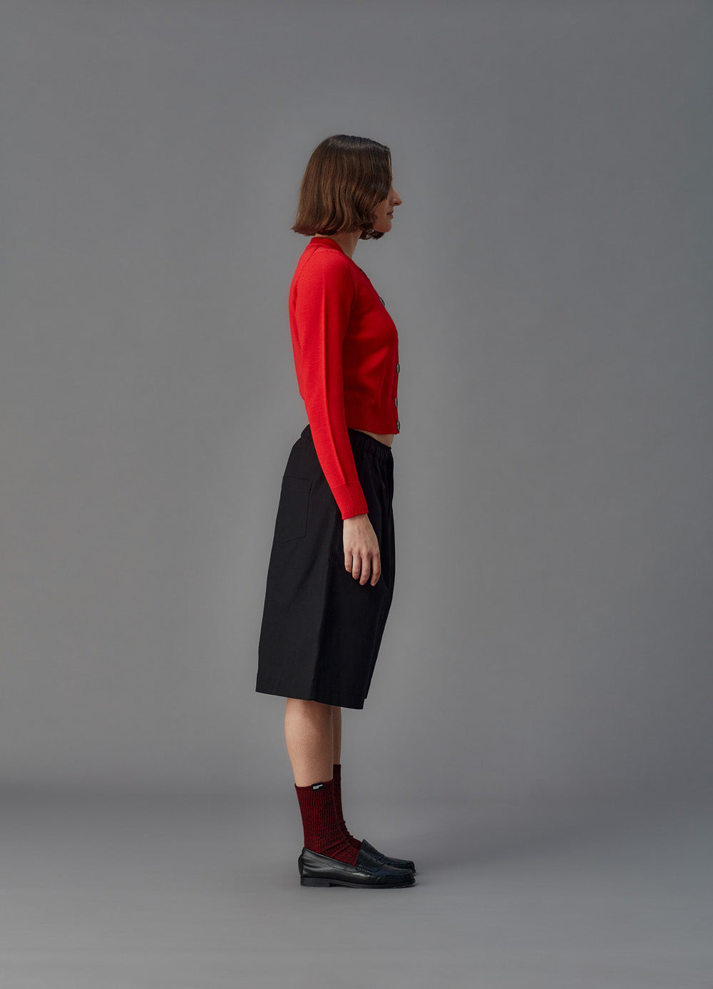 Person wearing a red sweater and black shorts on a gray background