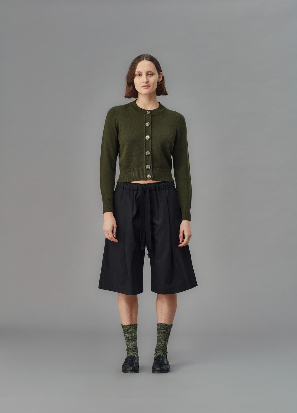 Person wearing a green cardigan and black shorts on a gray background