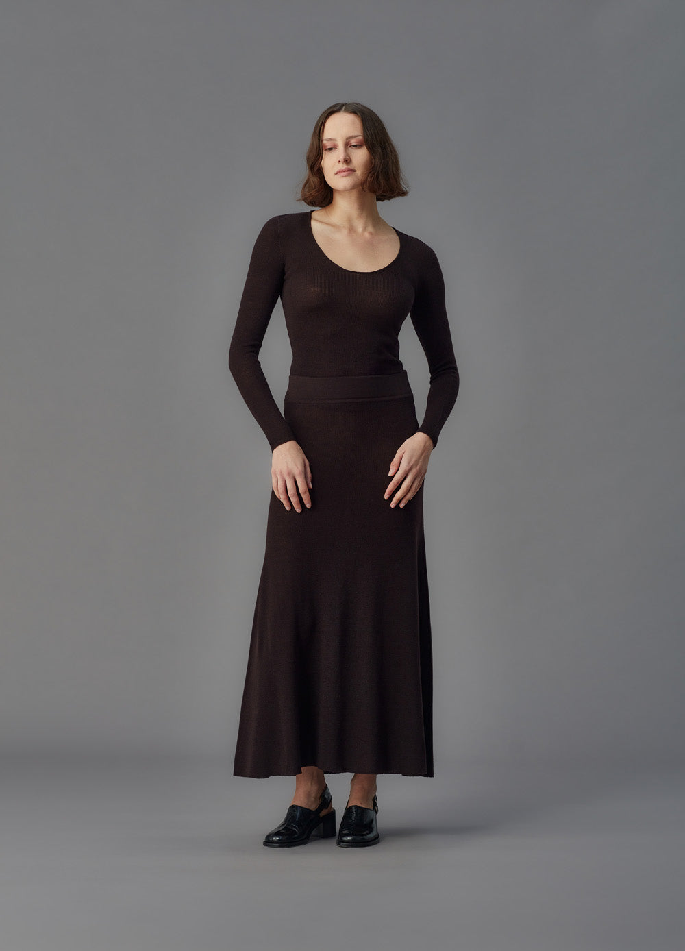 Woman wearing a u top and brown skirt against a gray background