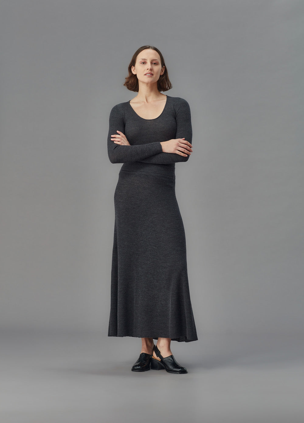 Woman wearing a long dark gray skirt and u top against a gray background
