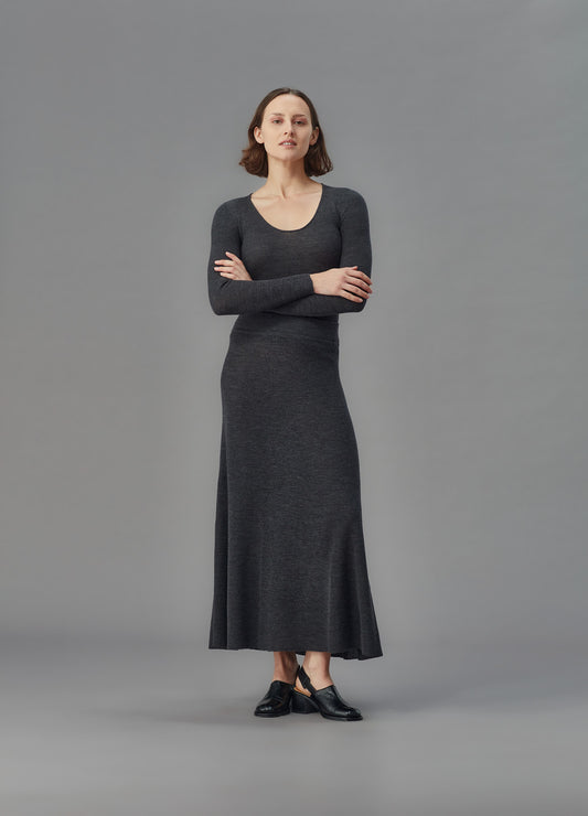 Woman wearing a long dark gray skirt and u top against a gray background