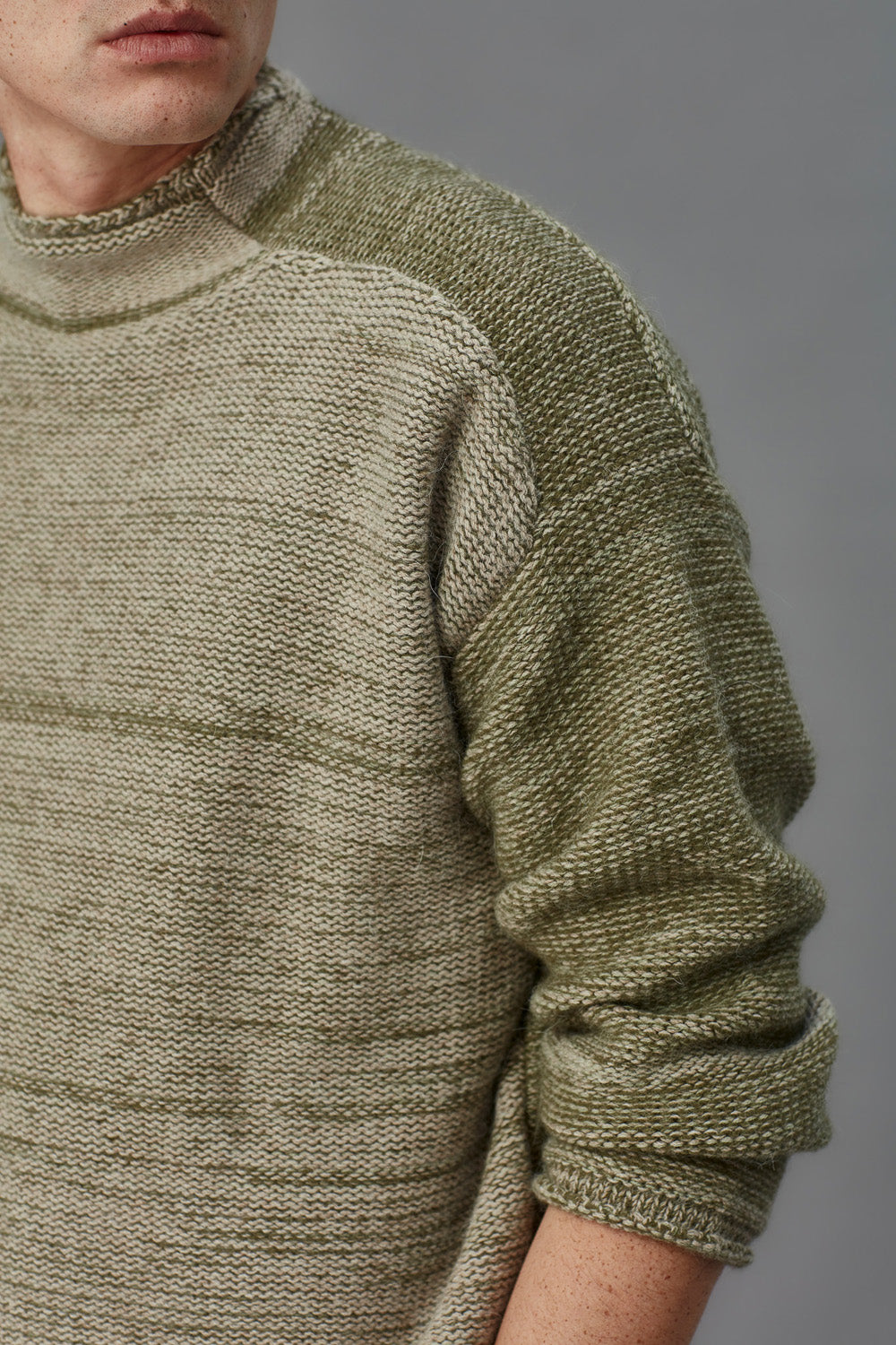 Close-up of a person wearing a textured green sweater against a gray background