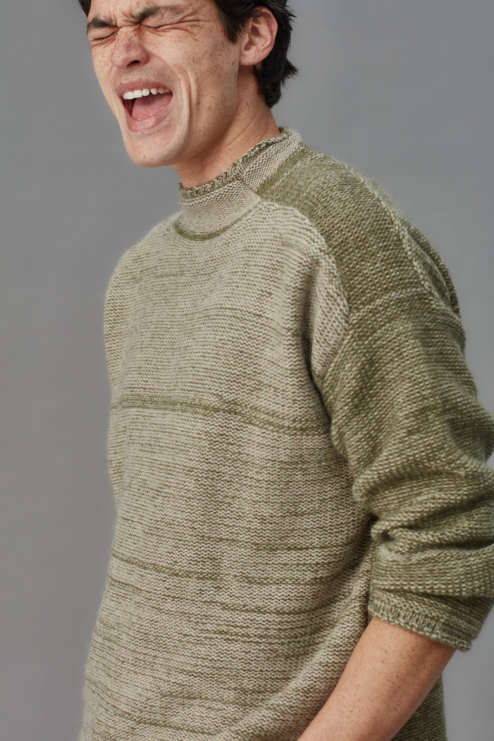 Man wearing a green knitted sweater against a gray background