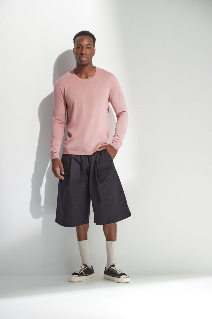Man wearing a pink long-sleeve shirt and black shorts against a white background
