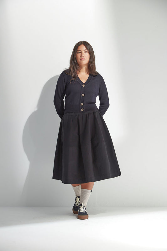 Woman wearing a dark navy V Neck Cardigan with a black skirt buttons on a white background