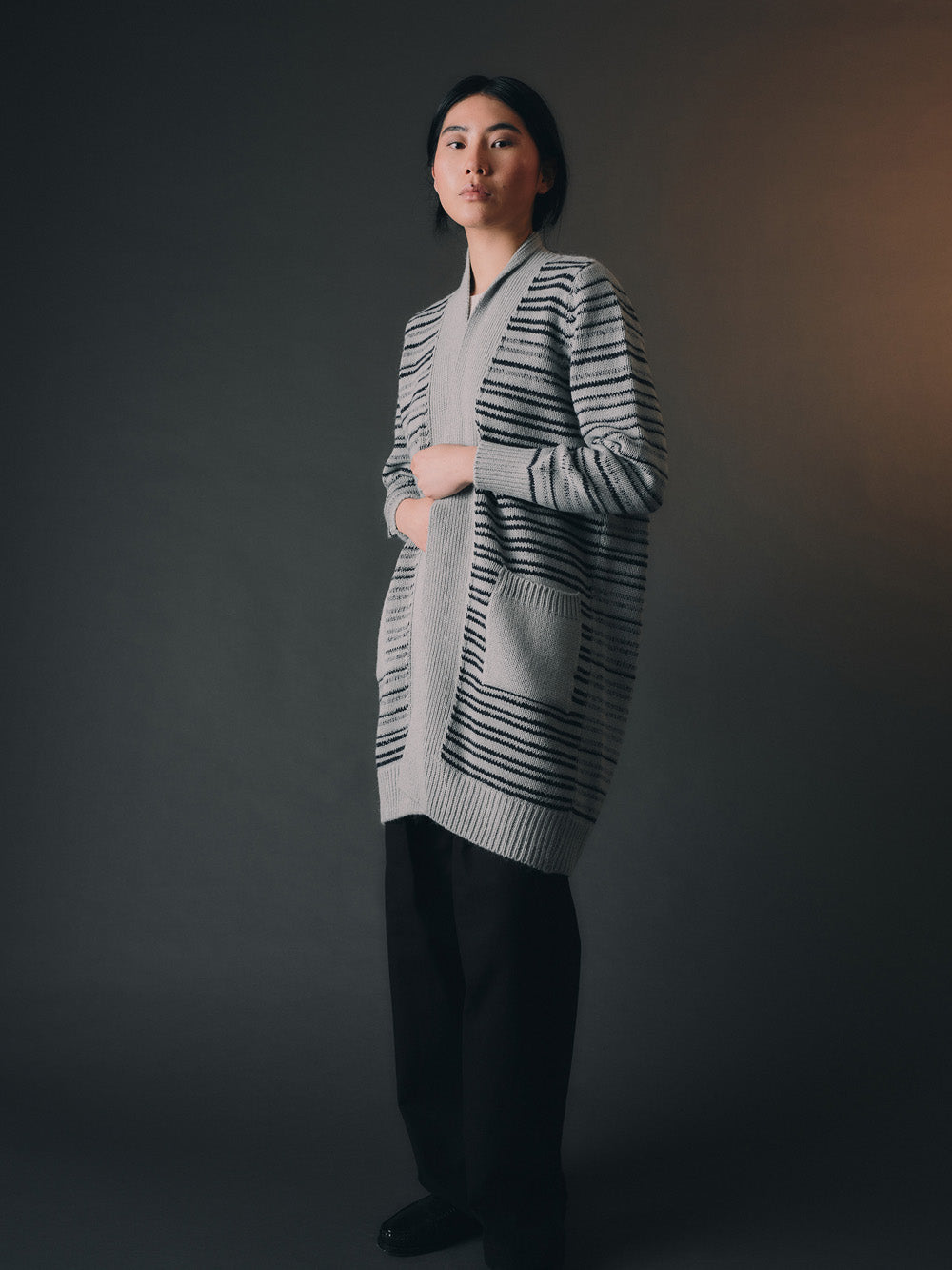 Woman wearing a long, stripe-patterned cardigan against a dark background