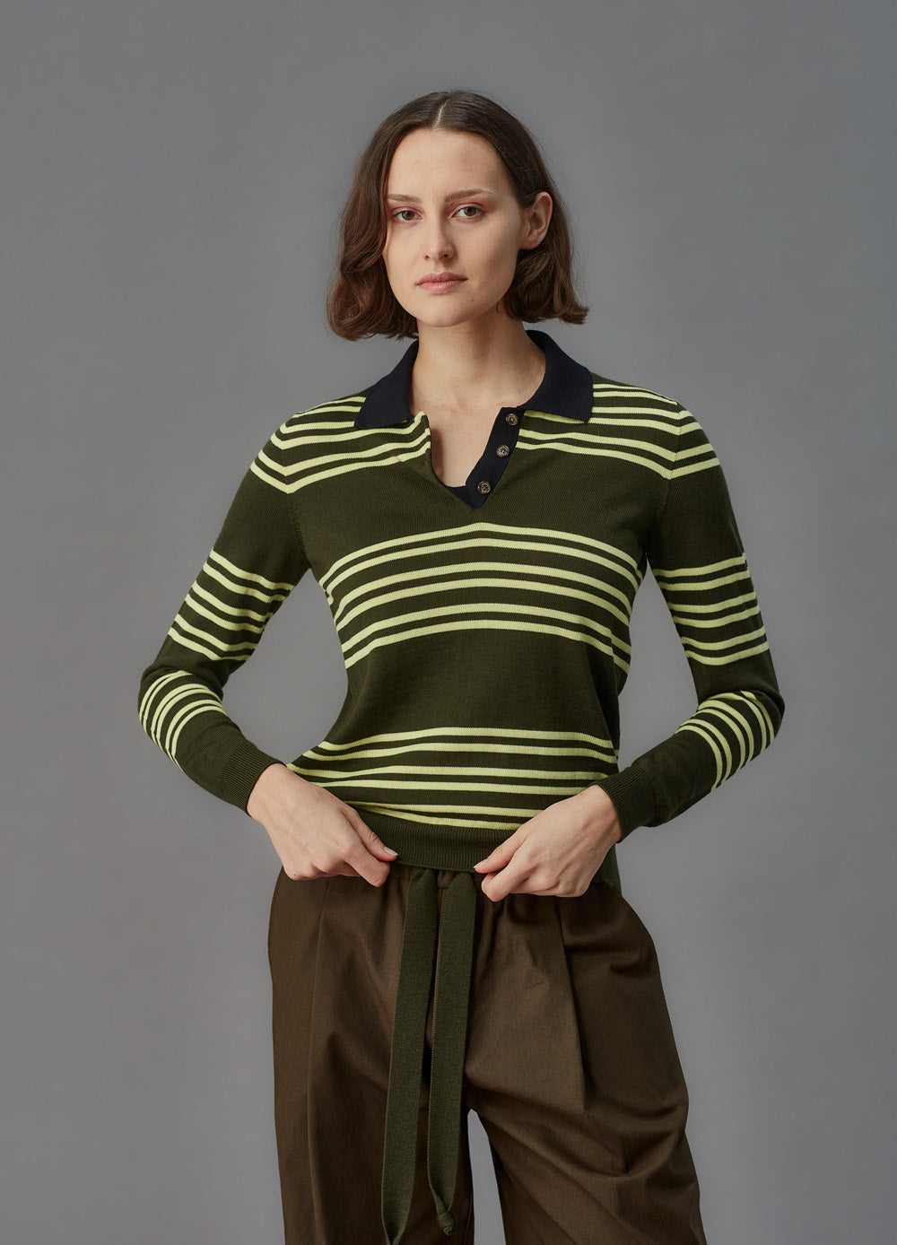 Woman wearing a green and yellow striped sweater with a gray background