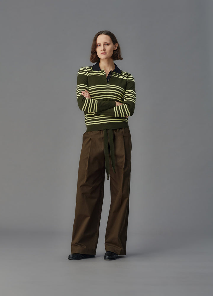 Woman wearing a brown and yellow striped sweater with brown pants on a gray background