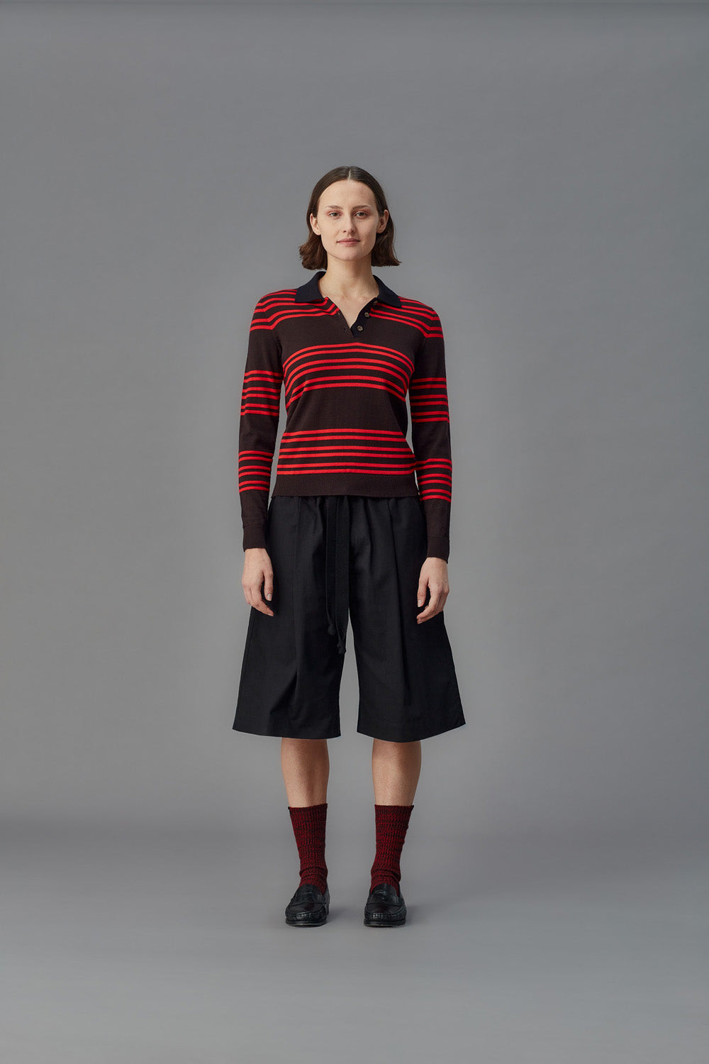 Person wearing a striped sweater and black pants on a gray background