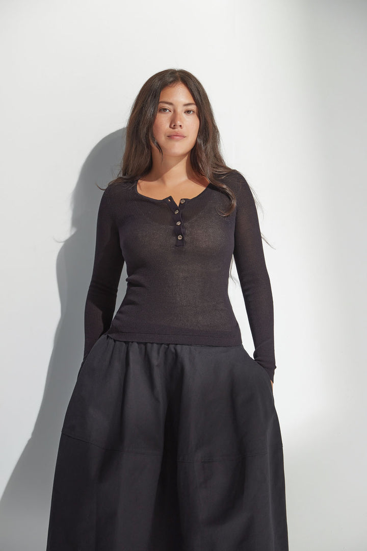 Woman wearing a dark long-sleeve top and black skirt against a white background