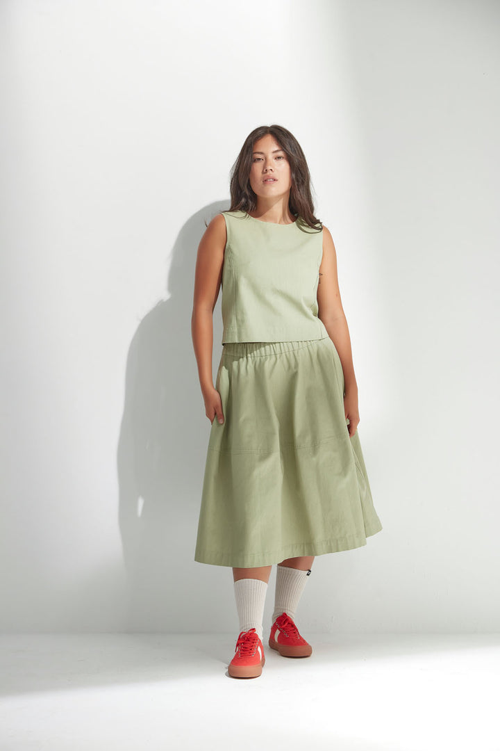 Woman wearing a light green sleeveless top and skirt with red shoes on a white background