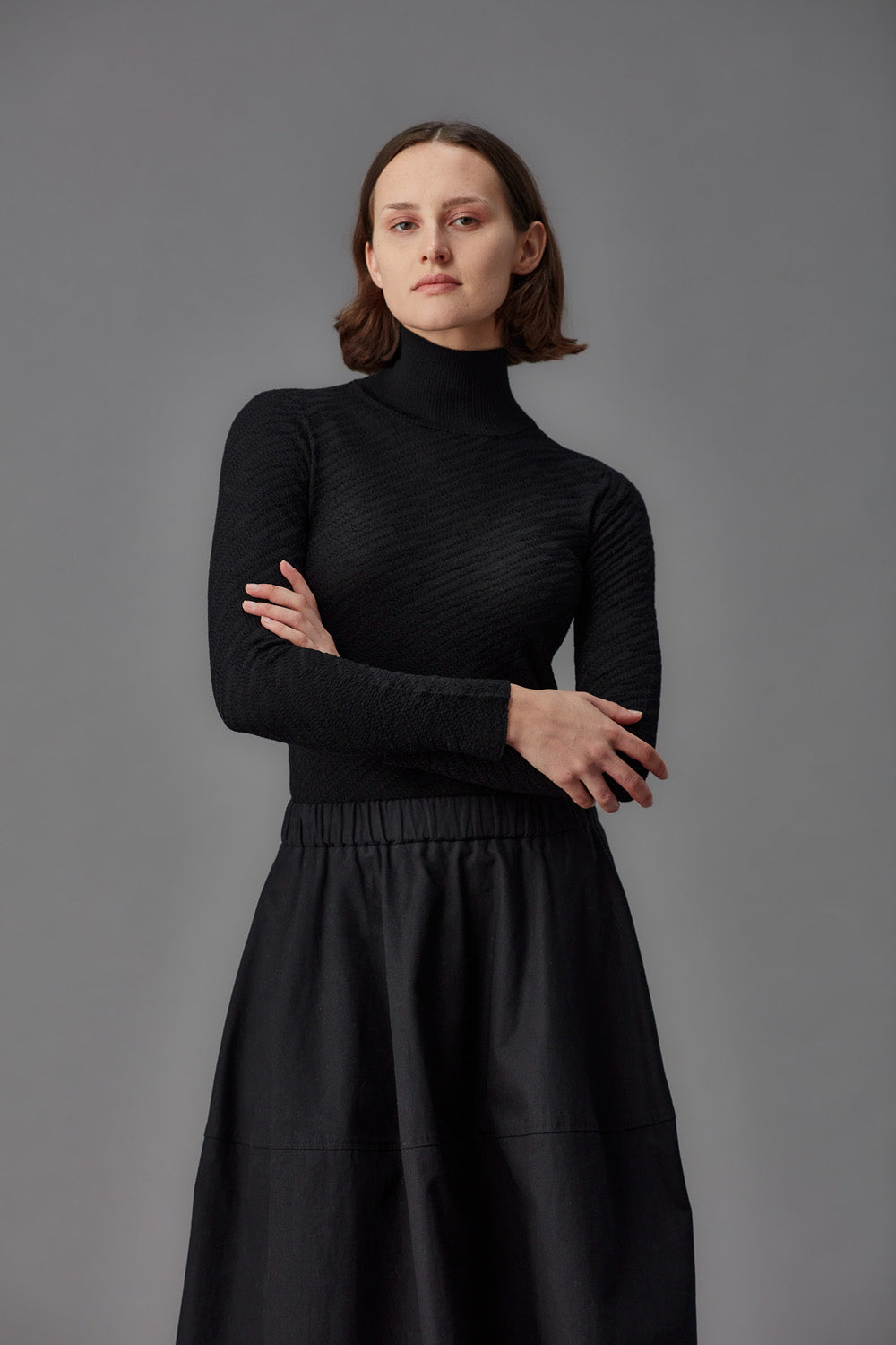 Person wearing a black turtleneck and skirt set against a gray background