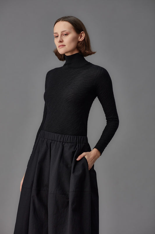 Woman wearing a black turtleneck and black skirt against a gray background