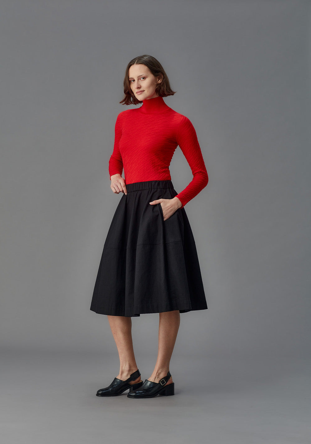 Woman wearing a red turtleneck and black skirt on a gray background