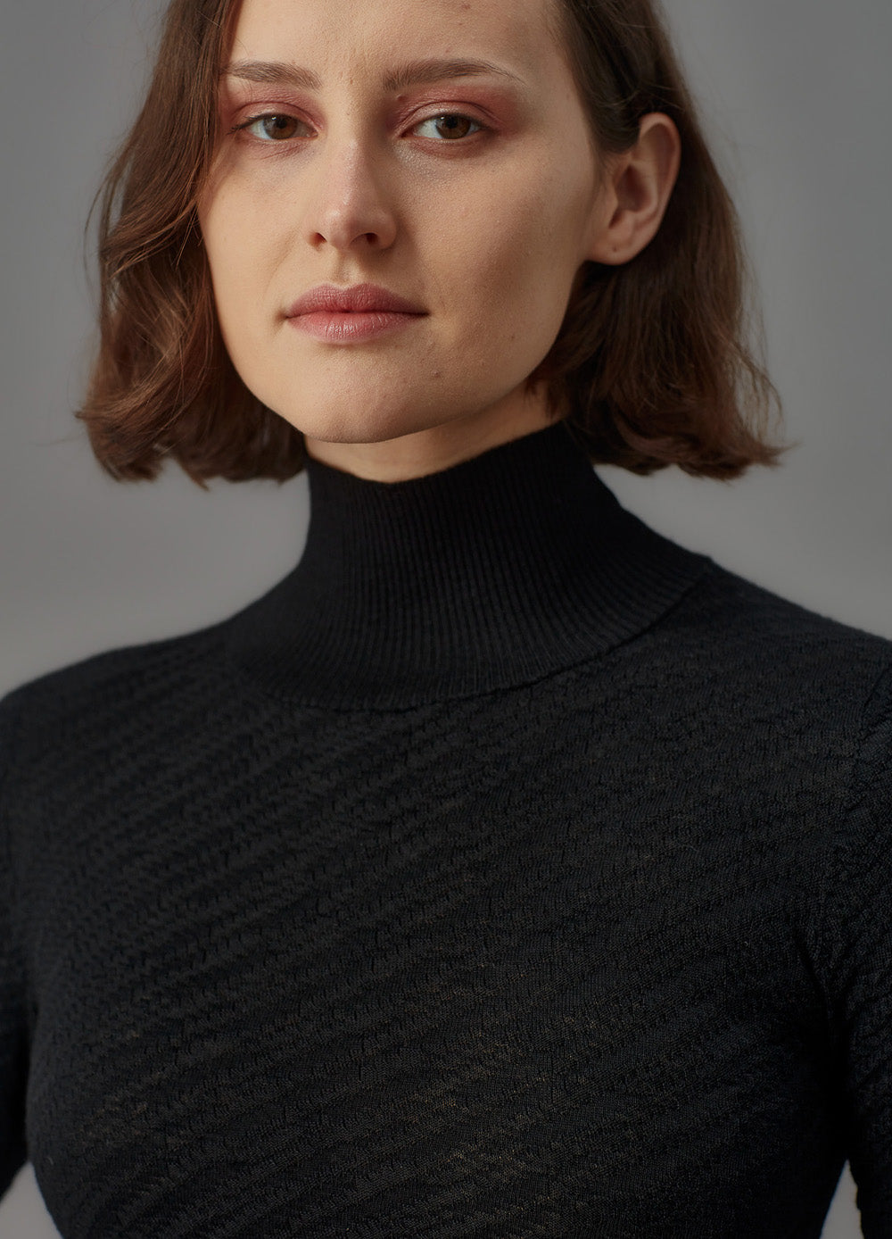 Woman wearing a black turtleneck dress against a gray background