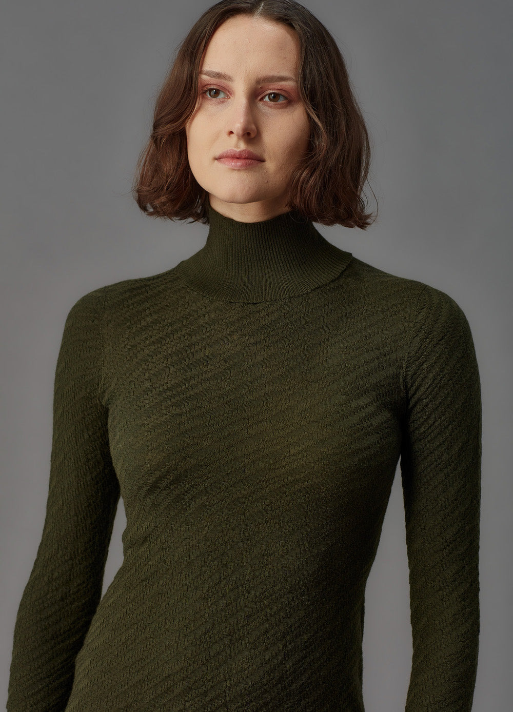 Woman wearing a green ribbed turtleneck dress against a gray background