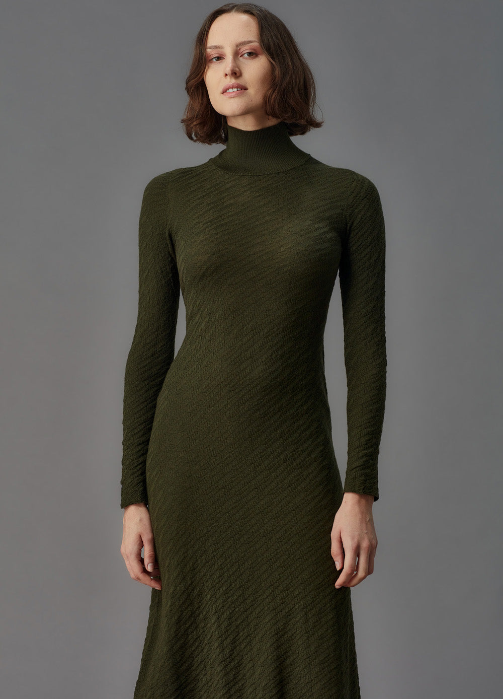 Woman wearing a green ribbed dress against a gray background