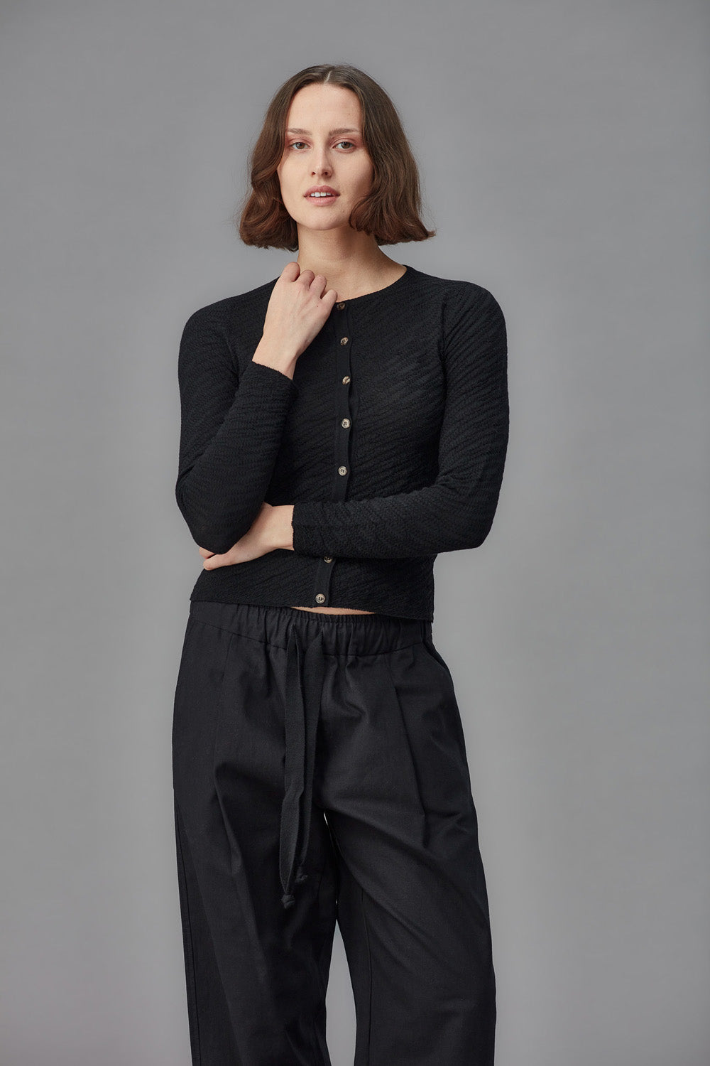 Woman wearing a black cardigan and black pants against a gray background