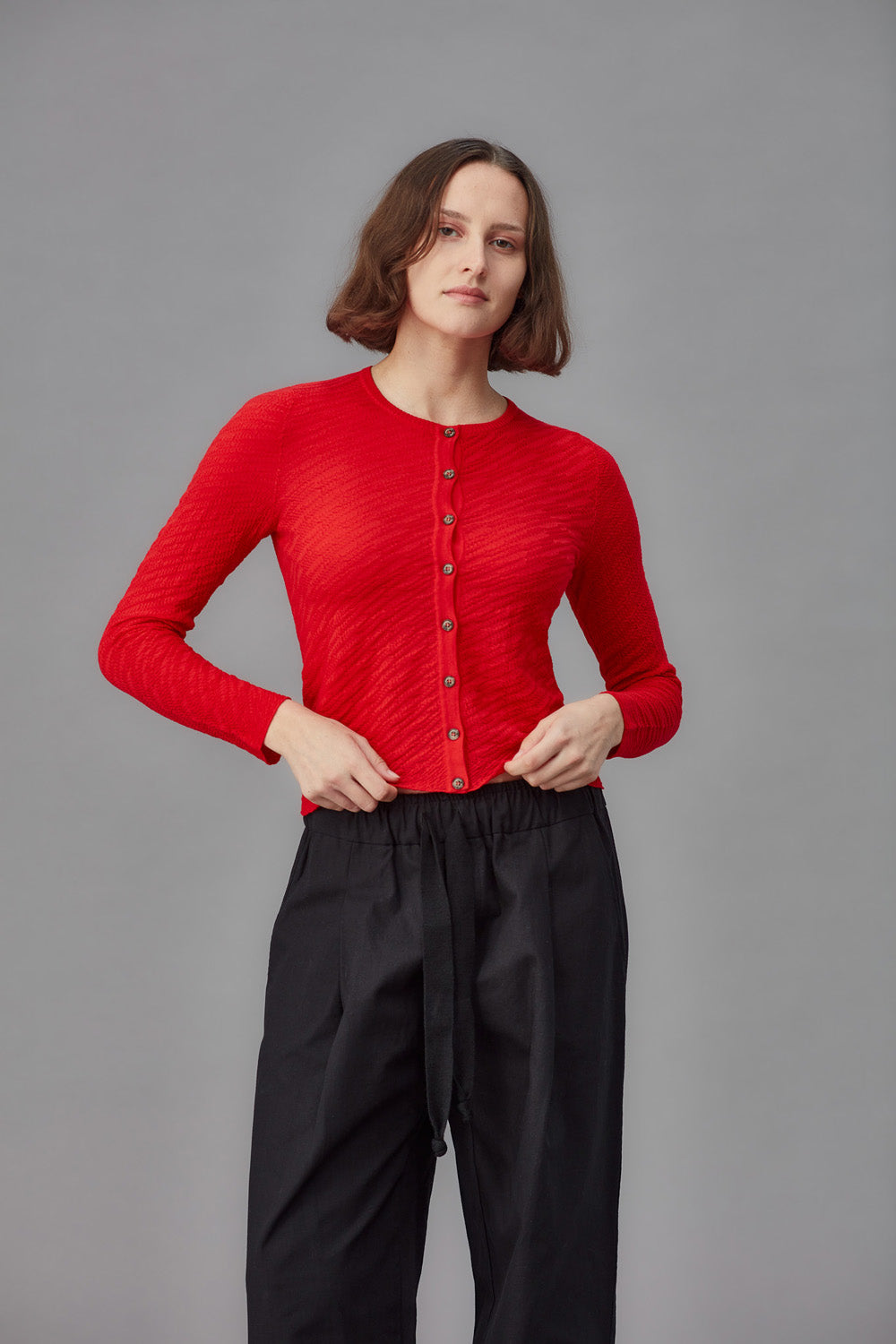 Woman wearing a red cardigan and black pants against a gray background