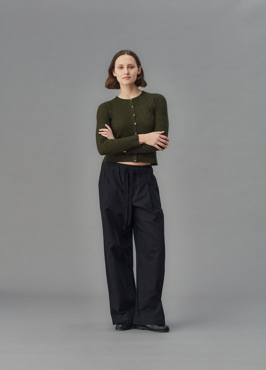 Person wearing a green cardigan and black pants on a gray background