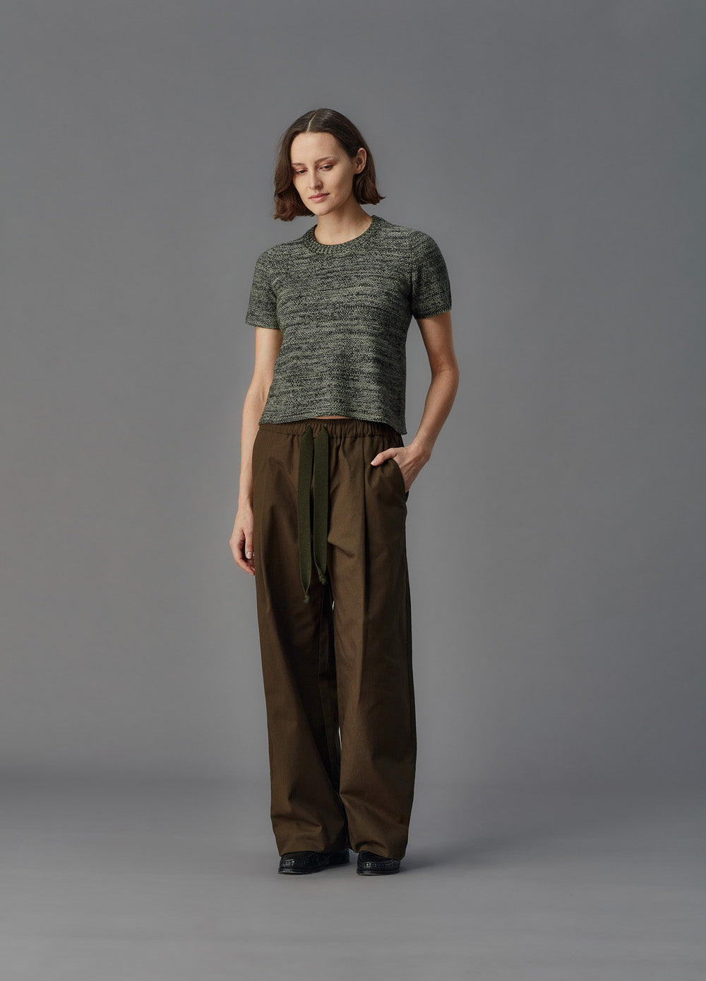 Person wearing a green shirt and brown pants against a gray background