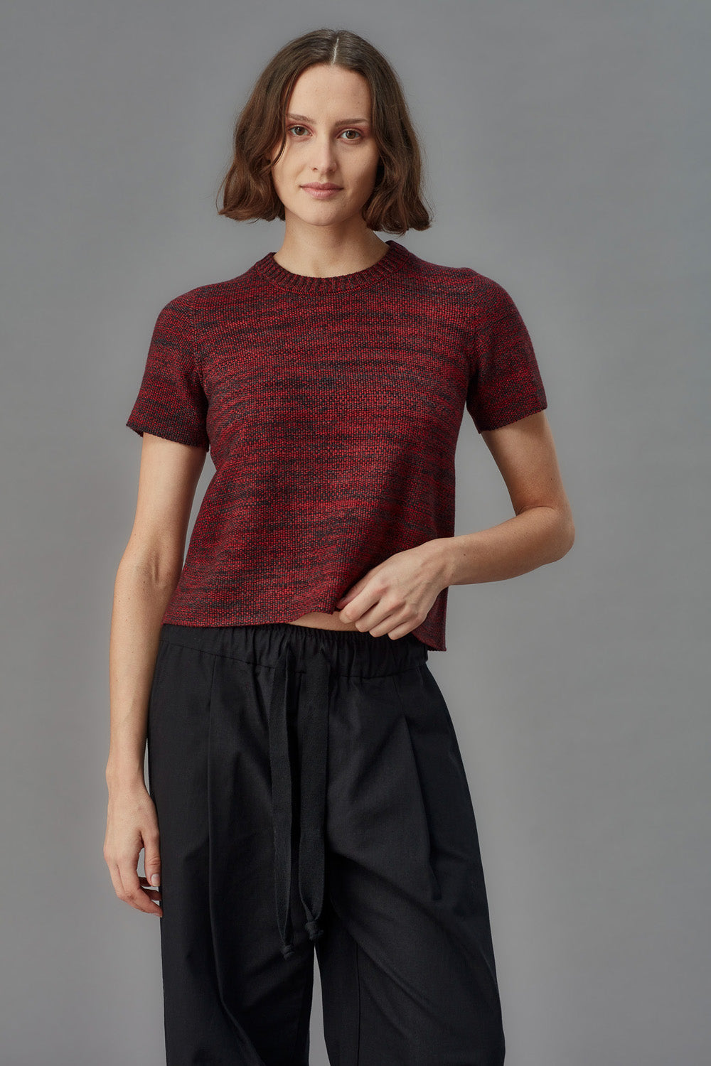 Woman wearing a red and black patterned shirt with black pants on a gray background