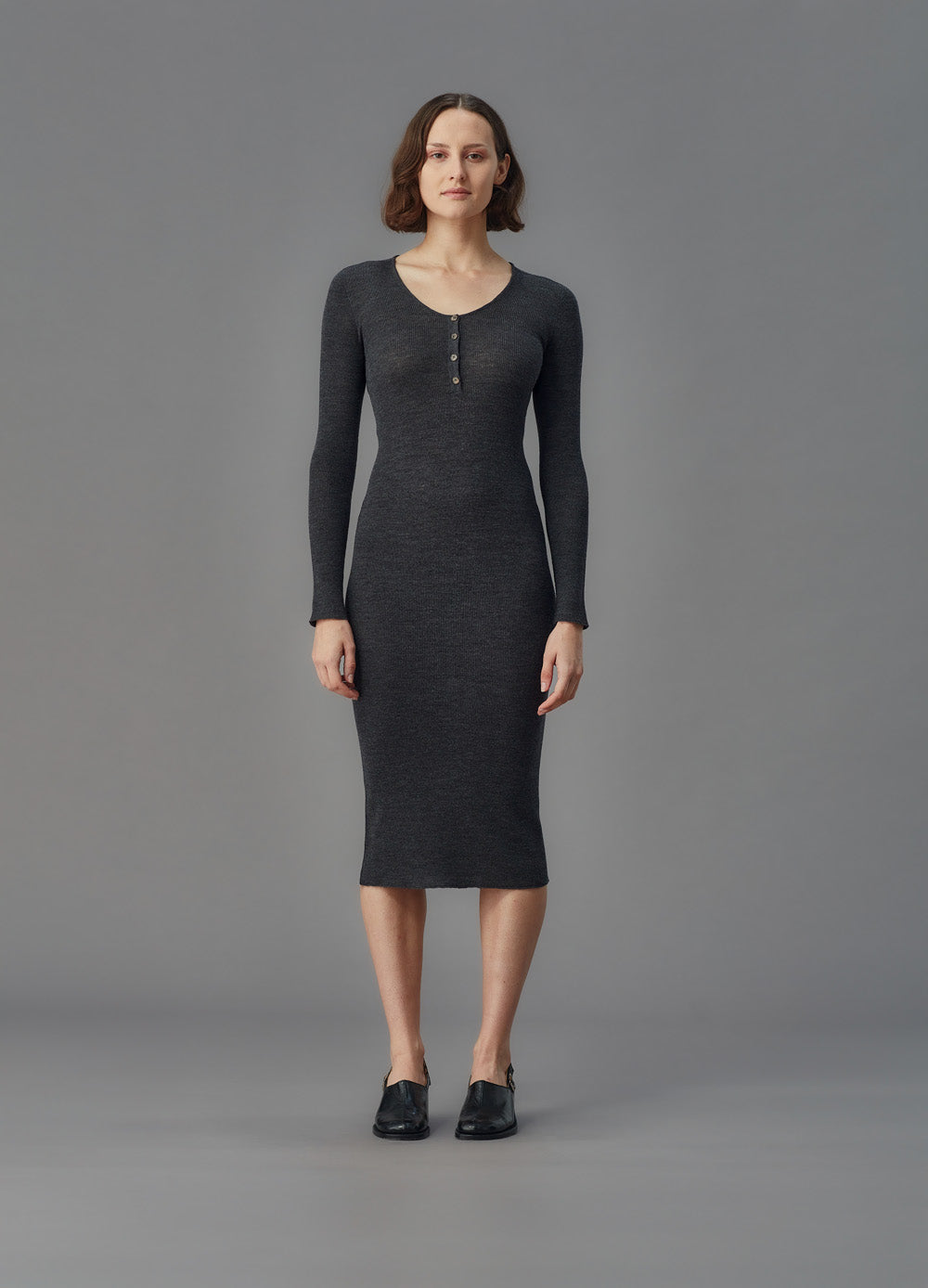 Woman wearing a dark gray long-sleeve dress against a gray background