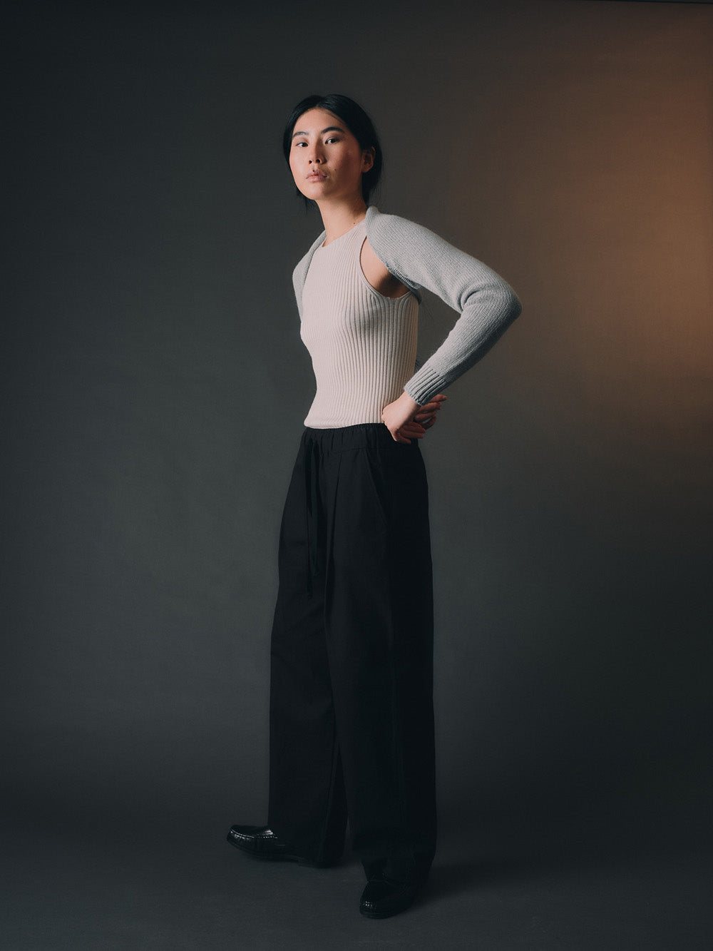 Woman wearing a light blue bolero sleeves over a beige top, standing against a light-colored wall.